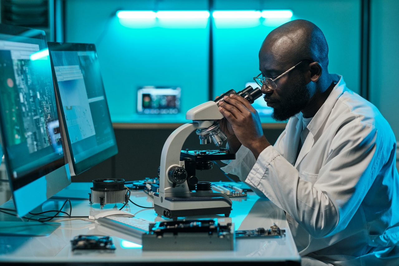 Young serious male researcher in whitecoat looking in microscope